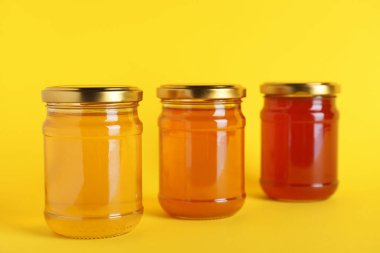 Sarı zemin üzerinde farklı türde organik bal bulunan kavanozlar.