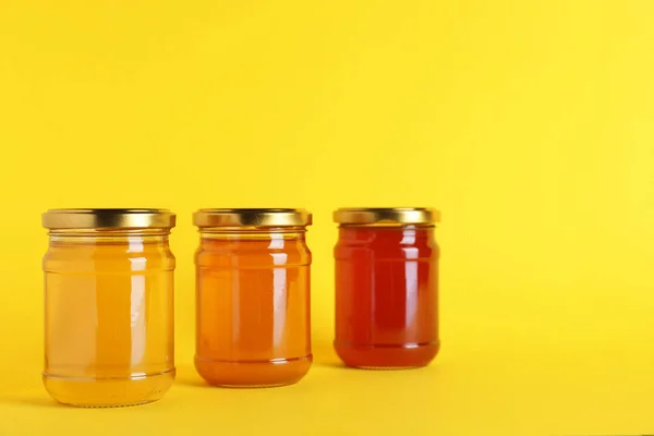 Баночки з різними видами органічного меду на жовтому фоні — стокове фото