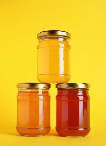 Jars with different types of organic honey on yellow background — Stock Photo, Image