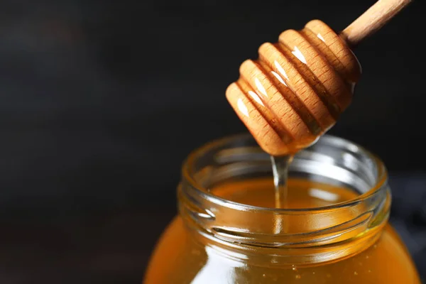 Tarro de miel orgánica y cazo sobre fondo oscuro, primer plano — Foto de Stock