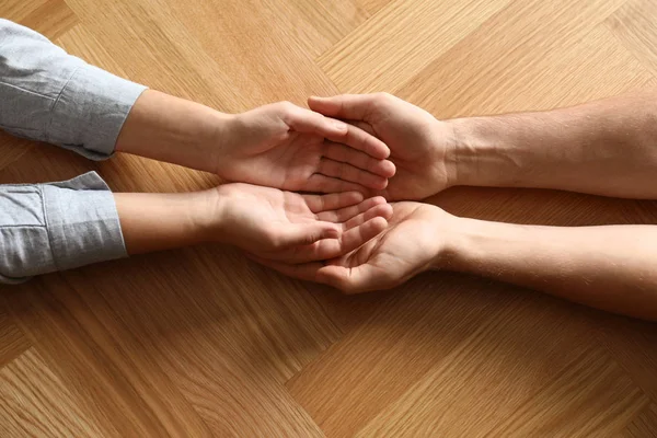 Young people holding hands on wooden background, top view. Happy family