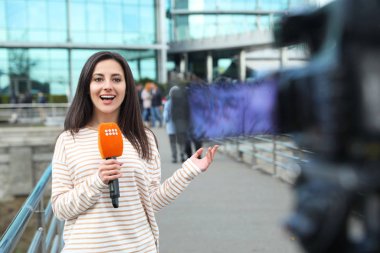 Mikrofonlu genç bayan gazeteci şehir sokaklarında çalışıyor.