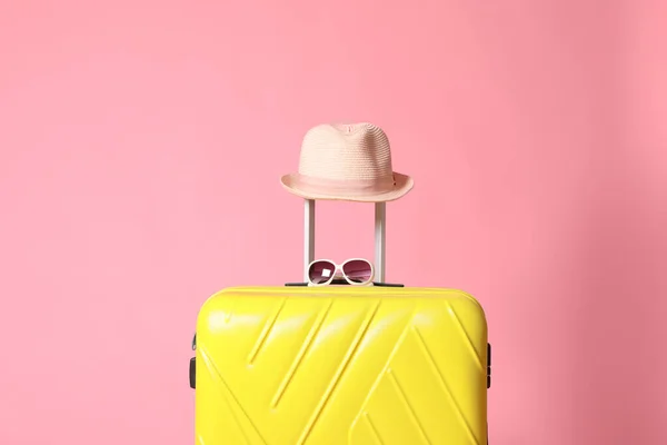Żółta walizka w okularach przeciwsłonecznych i kapeluszu na różowym tle — Zdjęcie stockowe