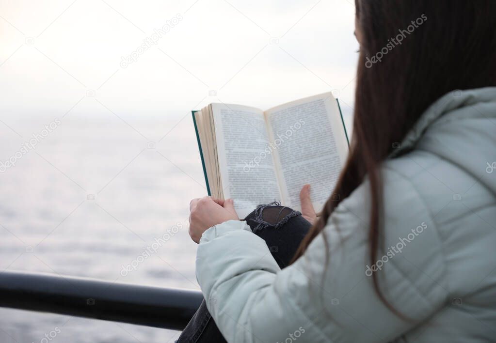 Woman reading book near river on cloudy day