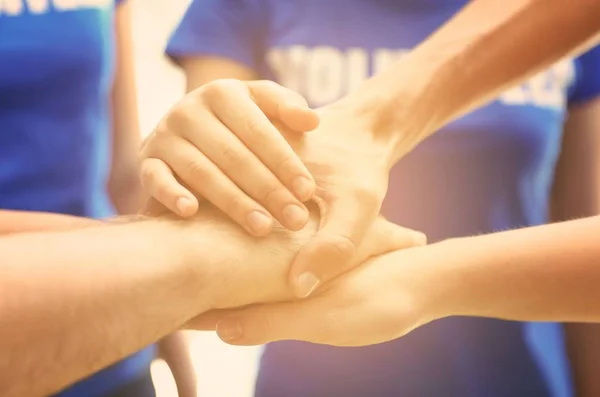 Group of volunteers joining hands together in sunlit room, closeup