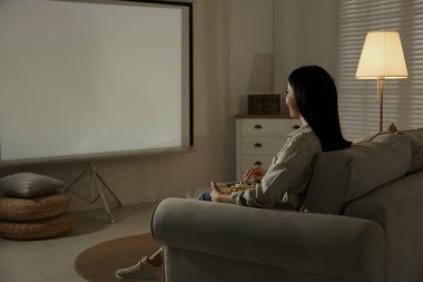 Evde video projektörü kullanan genç bir kadın film izliyor.