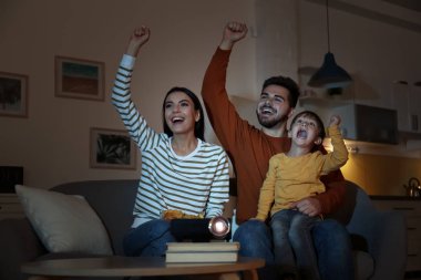 Evde video projektörü kullanarak televizyon izleyen duygusal aile.