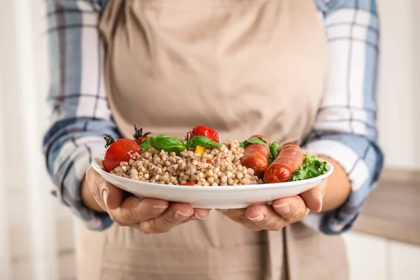 Woman holding plate with tasty buckwheat porridge and sausages, closeup