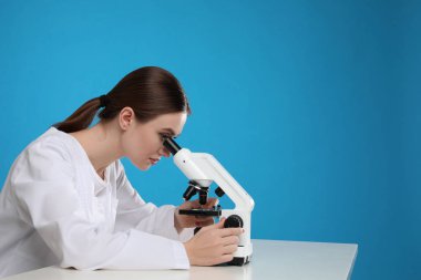 Bilim adamı masadaki modern mikroskobu mavi arka Grou 'ya karşı kullanıyor