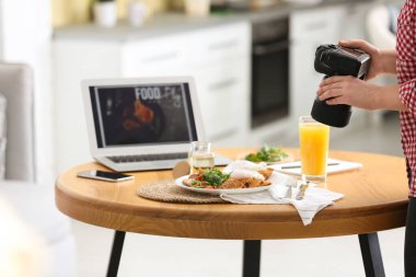 Yemek blogcusu öğle yemeğini içeride, ahşap masada çekiyor.