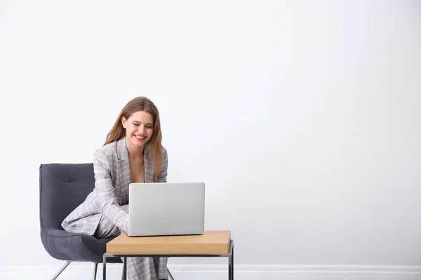 Giovane donna che lavora con il computer portatile in poltrona all'interno. Spazio per t — Foto Stock