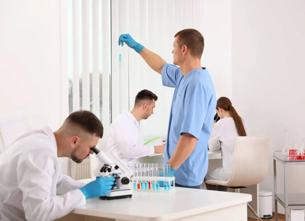 Científico usando microscopio en la mesa y colegas en el laboratorio —  Fotos de Stock