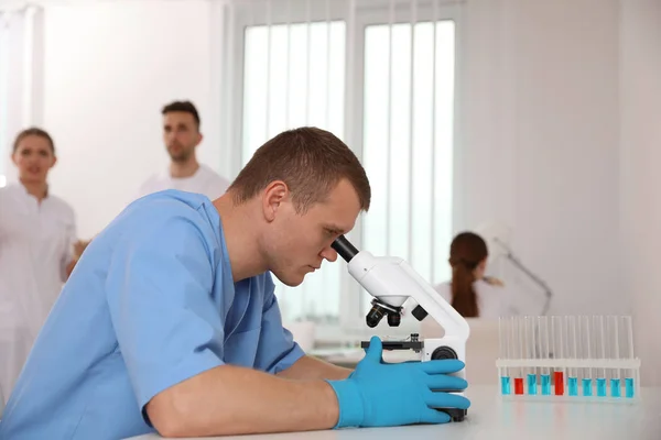 Científico usando microscopio en la mesa y colegas en el laboratorio — Foto de Stock