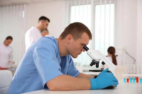 Científico usando microscopio en la mesa y colegas en el laboratorio — Foto de Stock