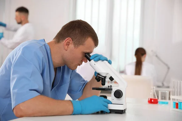 Wissenschaftler mit Mikroskop am Tisch und Kollegen im Labor — Stockfoto