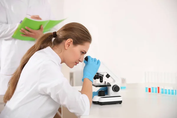 Vědec používající mikroskop u stolu a kolega v laboratoři. — Stock fotografie