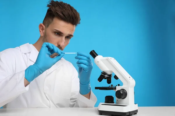 Человек с слайдом и микроскопом за белым столом на синем фоне . — стоковое фото