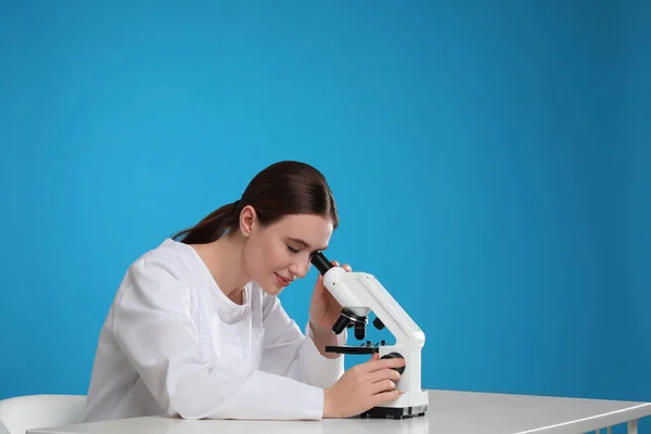 Vědec pomocí moderního mikroskopu u stolu proti modrému pozadí — Stock fotografie