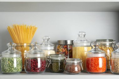Cam kavanozlar ve beyaz rafta değişik şekillerde makarna.