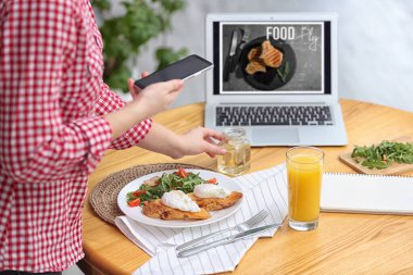 Yemek blogcusu öğle yemeğini içeride, ahşap masada çekiyor.