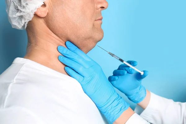 Mature man with double chin receiving injection on blue backgrou