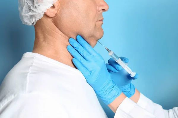 Mature man with double chin receiving injection on blue backgrou