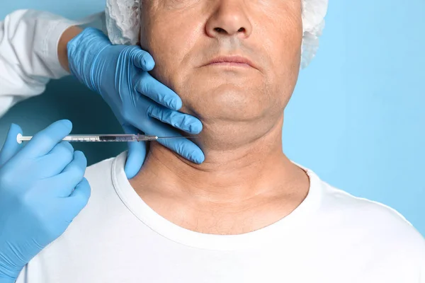 Starší muž s dvojitou bradou dostává injekci na modrém pozadí — Stock fotografie