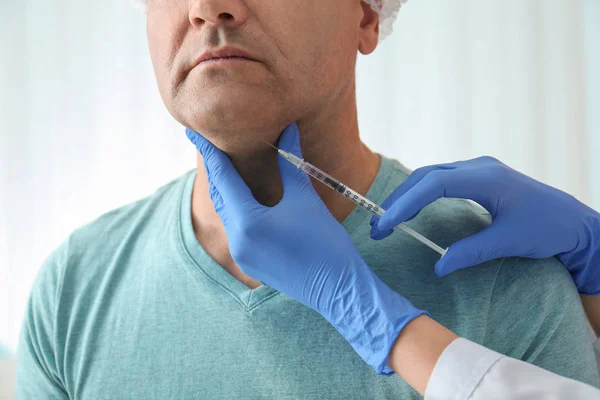 Mature man with double chin receiving injection in clinic, close