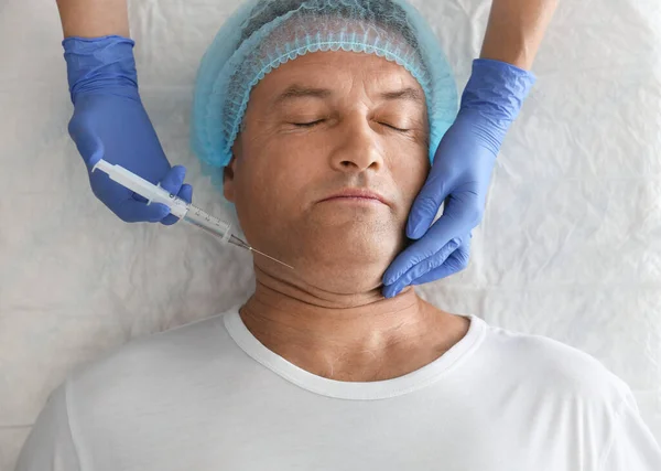 Mature man with double chin receiving injection in clinic, above