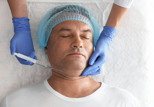 Mature man with double chin receiving injection in clinic, above