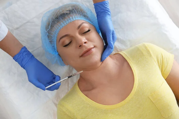 Mature woman with double chin receiving injection in clinic, abo