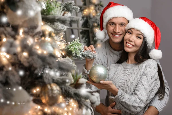 Šťastný mladý pár v Santa klobouky zdobení vánoční strom toget — Stock fotografie