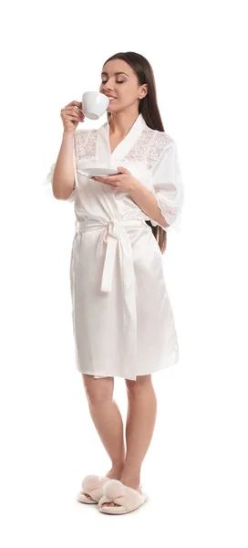Giovane donna in vestaglia di seta con tazza di bevanda su backgroun bianco — Foto Stock