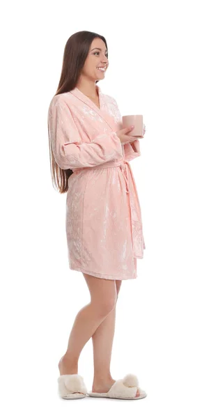 Jovem mulher em roupão de banho com xícara de bebida no fundo branco — Fotografia de Stock