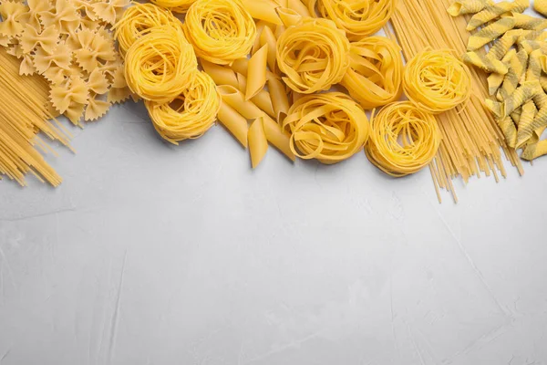 Diferentes tipos de pasta en la mesa gris claro, la puesta plana. Espacio fo — Foto de Stock