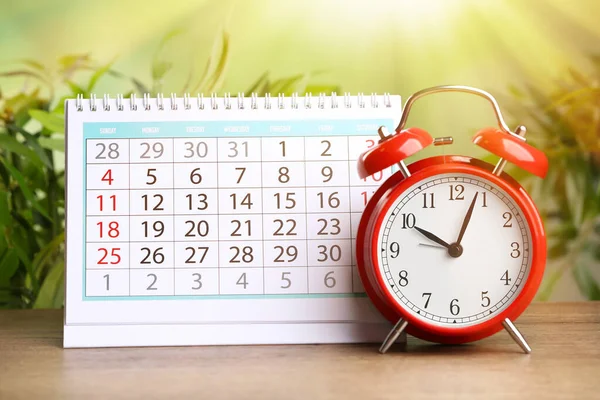 Календарь и будильник на деревянном столе против размытого зеленого цвета b — стоковое фото
