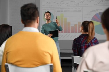 Erkek işletme eğitmeni konferans odasında projeksiyon ekranıyla konferans veriyor.