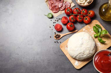 Gri masa üzerinde hamur ve malzemelerle düz kompozisyon, metin için boşluk. Pepperoni pizza tarifi.