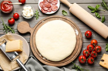 Hamurlu düz kompozisyon ve ahşap masada pepperonili pizza için taze malzemeler.