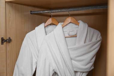 Ahşap dolapta asılı beyaz bornozlar.