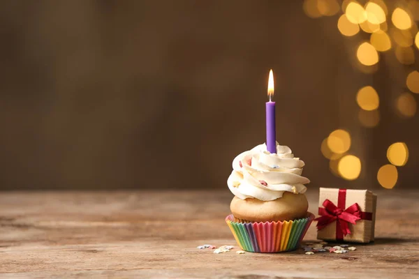 Кекс на день рождения со свечой и подарочной коробкой на деревянном столе — стоковое фото