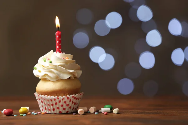 Birthday cupcake with candle on wooden table against blurred lig