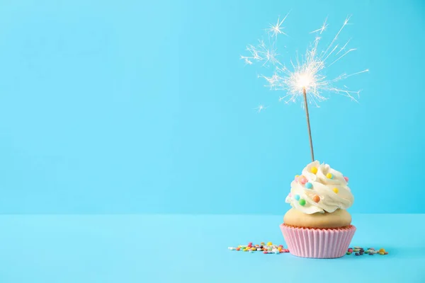 Birthday cupcake with sparkler on light blue background. Space f