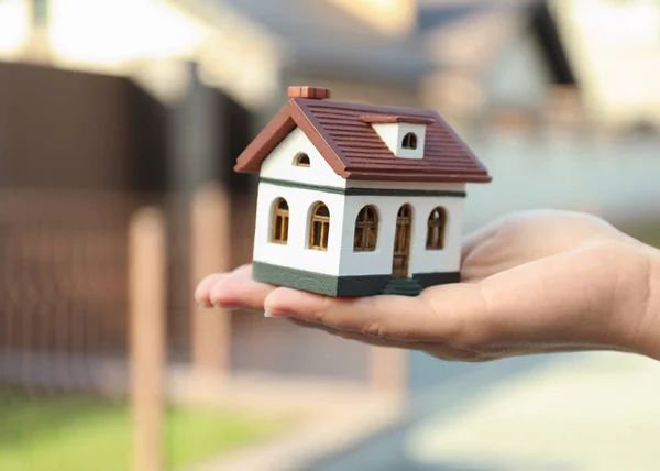 Real estate agent holding house model outdoors, closeup