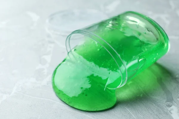 Wywrócony plastikowy pojemnik z zielonym śluzem na marmurowym tle — Zdjęcie stockowe