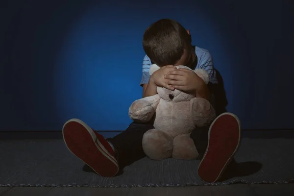 Rapazinho triste com ursinho perto da parede azul. Violência doméstica — Fotografia de Stock