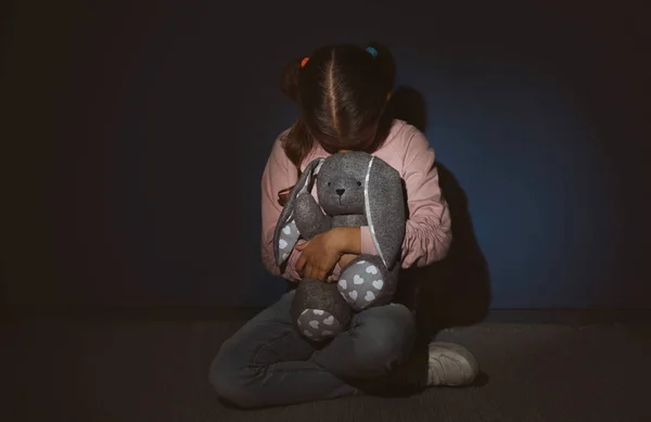Напуганная маленькая девочка с игрушкой возле голубой стены. Домашнее насилие — стоковое фото