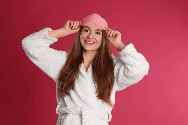 Jeune femme en peignoir et masque de sommeil pour les yeux sur fond cramoisi — Photo