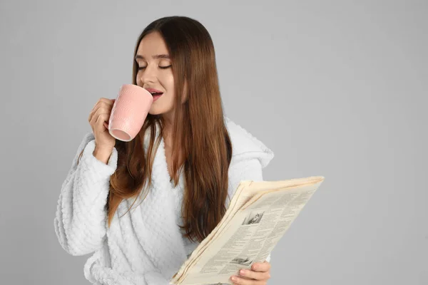 Krásná mladá žena v županu s šálkem kávy na světlo gr — Stock fotografie