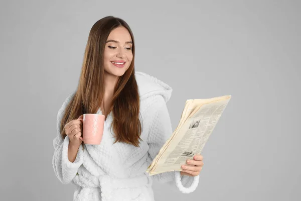 Krásná mladá žena v županu čtení novin na světlo žár — Stock fotografie